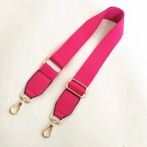 Détail d'une bandoulière rose fuchsia en toile avec boucles dorées et attaches en cuir