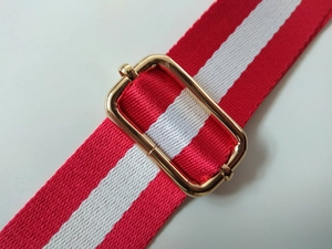 Detail of red and white striped nylon shoulder strap with a gold metal buckle