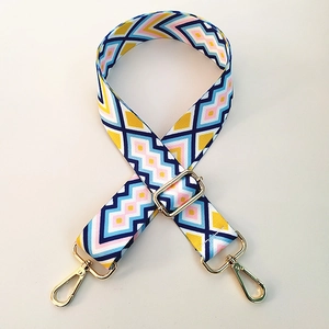 Adjustable geometric patterned bag strap with gold metal hooks on white background