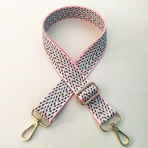 Detail of adjustable pink herringbone bag strap with blue texture and gold metal hooks