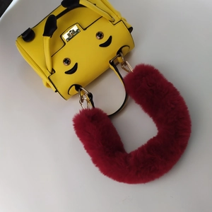 Detail of yellow handbag with cartoon smiley face and wine red faux fur handle accessory
