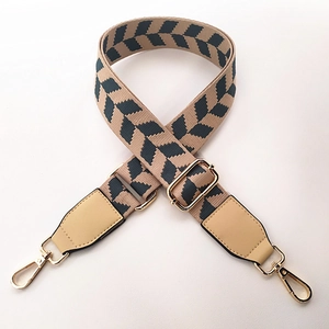 Close-up of adjustable beige canvas bag strap with chevron pattern and gold metal hooks