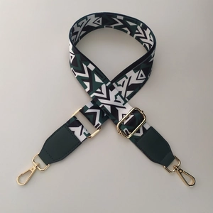 Close-up of geometric woven bag strap with green faux leather ends and gold hardware