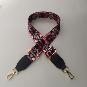 Macro detail of adjustable woven bag strap with red heart pattern and gold metal hooks