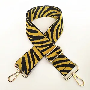 Détail d'une bandoulière zébrée noire et jaune avec des boucles en métal doré poli
