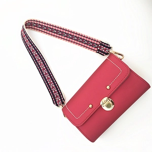 Detail of red leather square bag featuring embroidered geometric strap and gold buckle