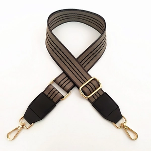 Detail of adjustable striped canvas bag strap with gold metal hooks and leather accents