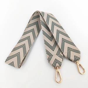 Close-up of wide embroidered canvas strap with green V-pattern and gold metal swivel clips