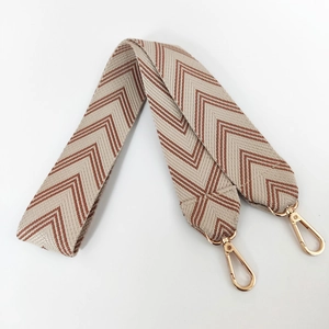 Close-up of wide canvas bag strap with brown herringbone pattern and gold metal hooks