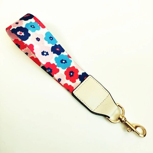 Detalle de correa de mano floral para bolso con cuero blanco y mosquetón dorado