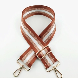 Detail of adjustable tan striped nylon bag strap with polished gold-tone metal buckles