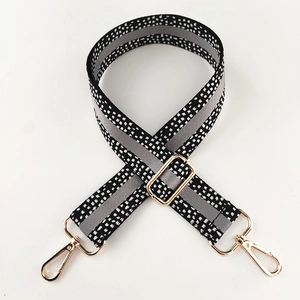 Detail of adjustable woven wide bag strap with black white pattern and gold metal hooks