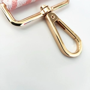 Macro shot of durable golden metal swivel lobster clasp with pink houndstooth woven strap