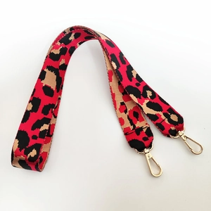 Détail de la bandoulière en nylon léopard rouge avec mousquetons dorés et tissage épais