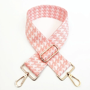 Macro detail of wide pink houndstooth woven bag strap with adjustable gold hardware