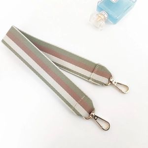 Detail view of woven striped bag strap with golden lobster clasps on white surface