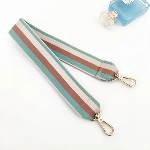 Detail of wide striped canvas shoulder strap with golden lobster clasps and blue perfume bottle