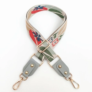 Detailed close-up of floral embroidered bag strap with grey leather ends and gold buckles