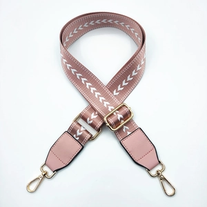 Close-up of pink nylon bag strap with white arrow pattern and golden metal hardware clips