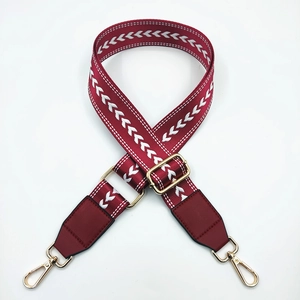 Detail of adjustable dark red nylon bag strap with white arrow embroidery and gold hooks