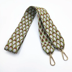 Close-up of embroidered wide bag strap with peacock pattern and golden lobster clasps