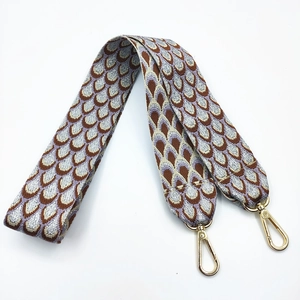 Close-up of wide jacquard bag strap with silver peacock embroidery and gold hooks