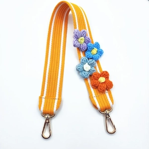 Close-up of woven orange striped strap with colorful crochet flowers and golden metal clasps