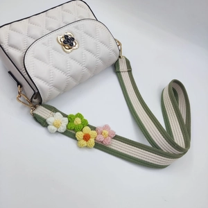 Detail of white quilted crossbody bag with colorful crochet floral strap and gold hardware
