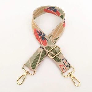 Detail of floral embroidery on wide canvas bag strap with golden metal lobster clasps
