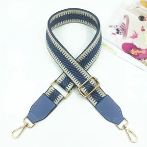 Macro detail of adjustable grey blue woven bag strap with golden metal hook and leather trim