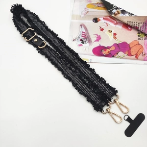 Detail of black canvas phone strap with fringe trim and golden metal lobster clasps