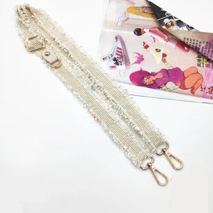 Detail of adjustable off-white woven crossbody strap with gold metal hooks and fringe edge