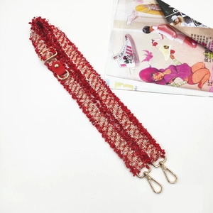 Detail of red and white tweed bag strap with fringe edges and golden swivel hooks