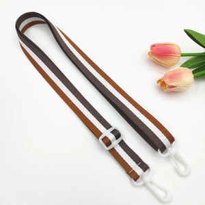 Detail of adjustable striped bag strap with brown and white nylon webbing and plastic hooks