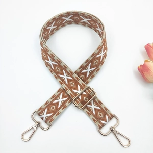 Close-up of geometric embroidered bag strap with gold metal lobster clasps on white background