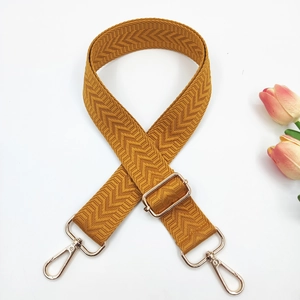 Detail of adjustable ginger yellow bag strap with V-shaped herringbone weave and gold buckle