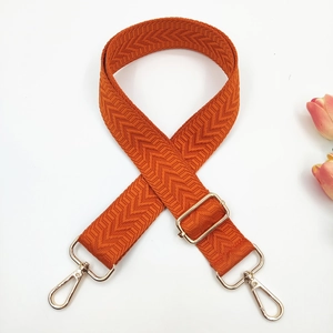 Close-up of orange woven bag strap with golden metal lobster clasps and herringbone pattern