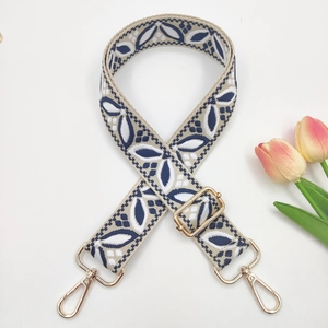 Close-up of embroidered bag strap with blue leaf patterns and golden metal hardware