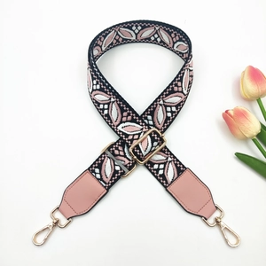 Close-up of pink and black ethnic embroidery on a wide bag strap with gold metal hooks