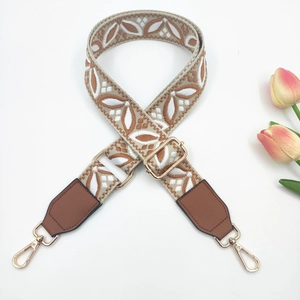 Detail of vintage geometric embroidery on wide woven crossbody bag strap with gold hooks