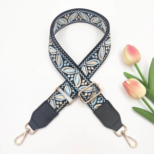 Detail of adjustable wide shoulder strap with blue floral embroidery and gold metal hardware