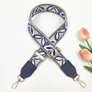 Detail of wide embroidered bag strap with blue leaf pattern and gold metal buckles