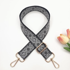 Macro detail of geometric black and white woven bag strap with golden metal lobster clasps