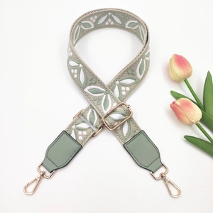Detail of green embroidered floral bag strap with gold metal buckles and leather ends