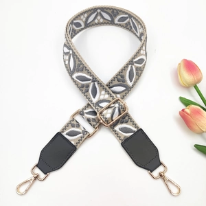 Detail of grey and white embroidered bag strap with gold metal hardware on white background