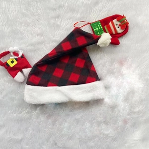Flat lay of red and black buffalo plaid Christmas hat and festive ornaments on white plush