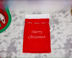 Detail of red plush Christmas gift bag with Merry Christmas embroidery and white pom-poms