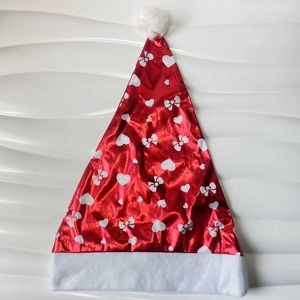 Detailed view of red glossy Christmas hat featuring white heart and bow patterns and fur trim