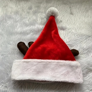 Flat lay of a red plush Christmas hat featuring brown reindeer antlers and a white pompom