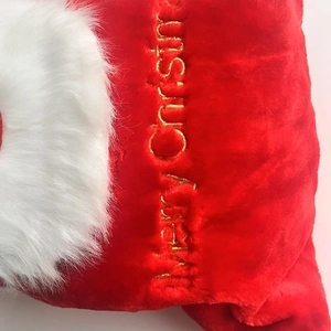 Detailed close-up of golden Merry Christmas embroidery on red plush holiday gift bag